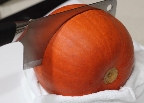 A pumpkin, wrapped at its base in a towel, with a meat cleaver halfway through.